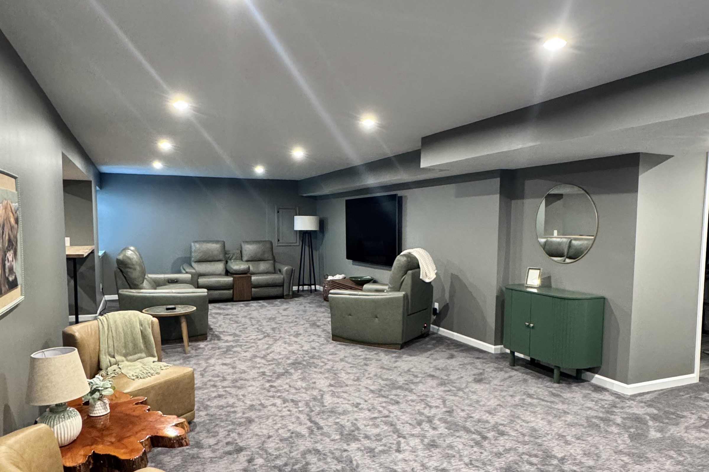 Finished basement lounge with recliners, a mounted television and a sage cabinet